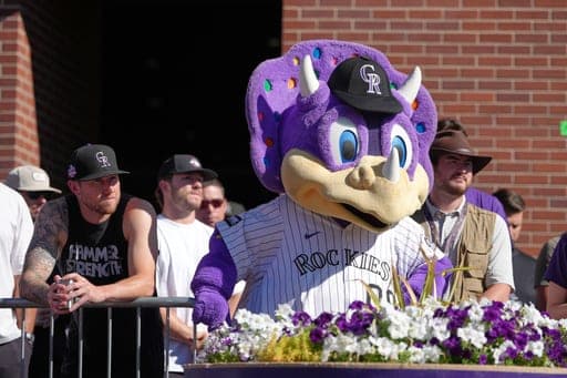 Colorado Rockies starting pitcher Kyle Feeland, left, joins team mascot Dinger the dinosaur in looking on as Baseball hall of famer and Rockies outfielder Larry Walker is honored by the unveiling of a statue of him in front of Coors Field Sunday, Aug. 23, 2026, in Denver. (AP Photo/David Zalubowski) (AP Photo/David Zalubowski)